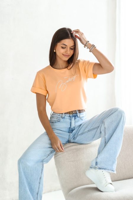 A világos barack színű, prémium minőségű ERICA Baby feliratos tavaszi rövid ujjú női pamut póló elasztikus anyaggal és fiatalos designnal a laza megjelenésért.