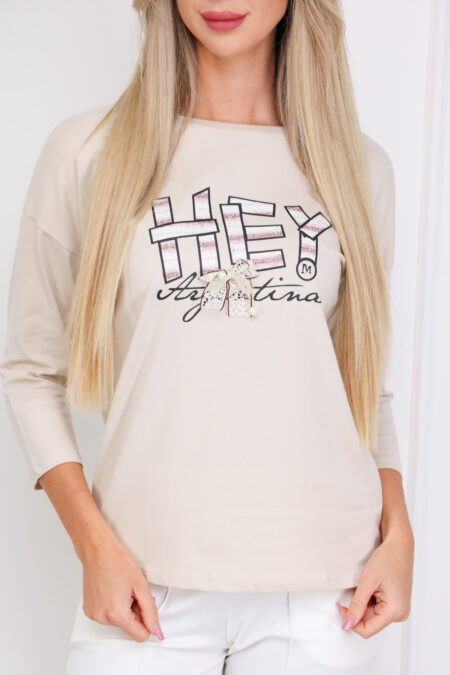 A bézs színű, divatos DORINA női tavaszi pamut felső elején található applikációnak és masninak hála különleges megjelenést kölcsönöz ennek a lezser felsőnek.