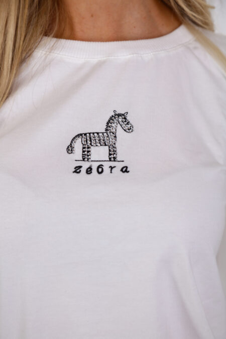 A fehér színű ZEBRA pamut nyári női felső kényelmes, puha tapintású pamut felső hímzett és strasszos zebradísszel – tökéletes választás stílusos nyári napokra.